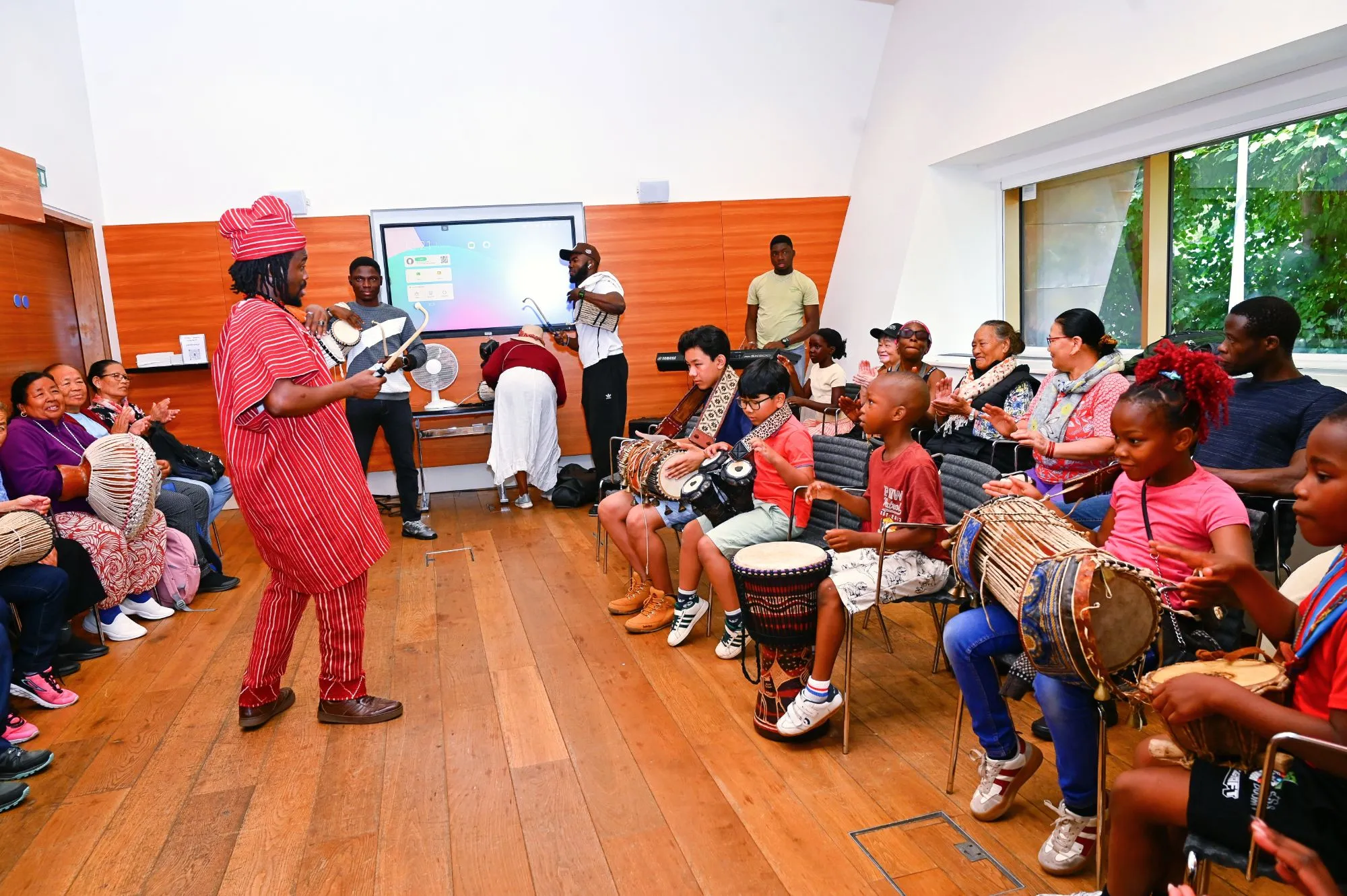 The founder leads a drum session as children and elders play and clap along