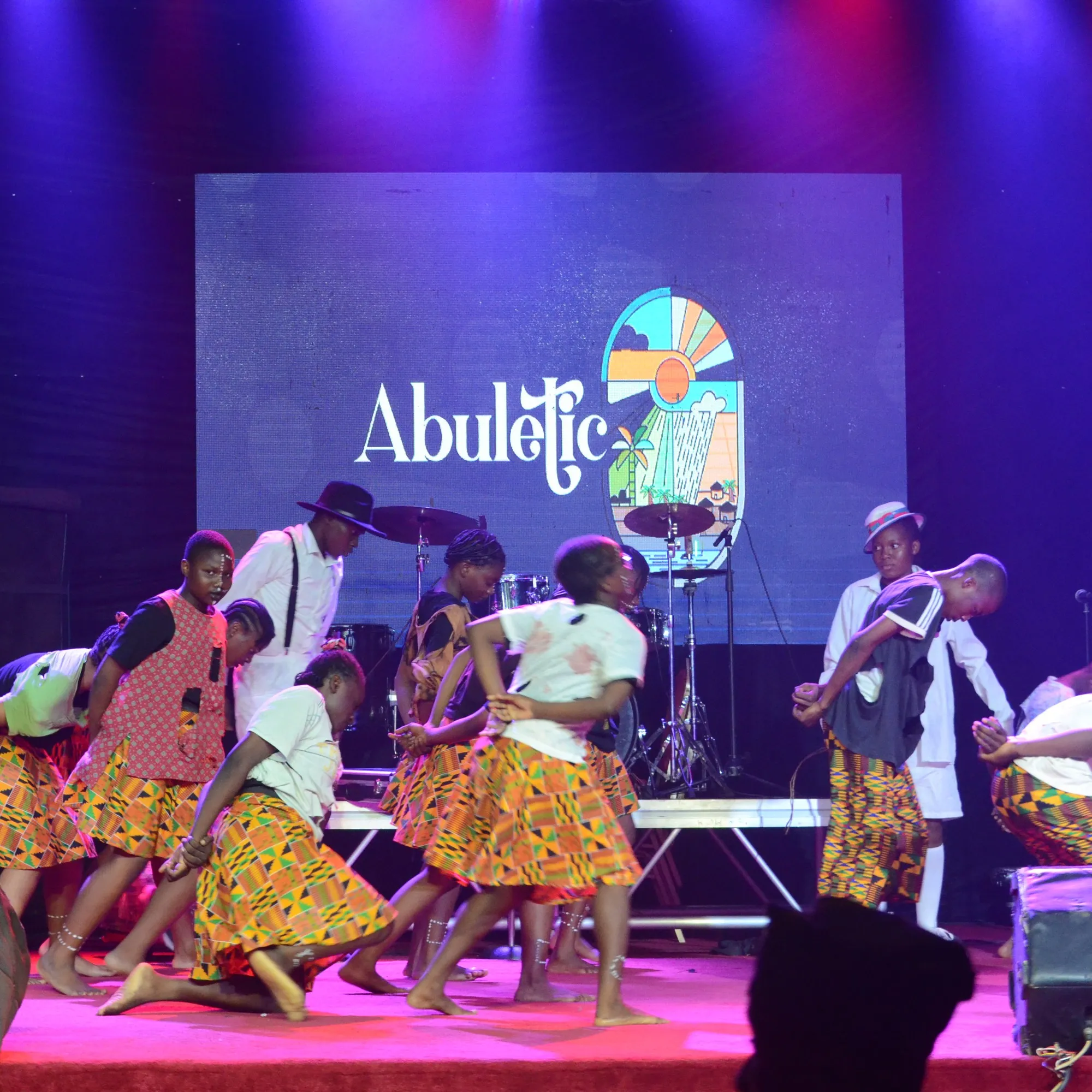 Young dancers in kente-print wrappers perform in front of the Abuletic logo at the Abuletic Tour Grand Finale, Abeokuta 2023